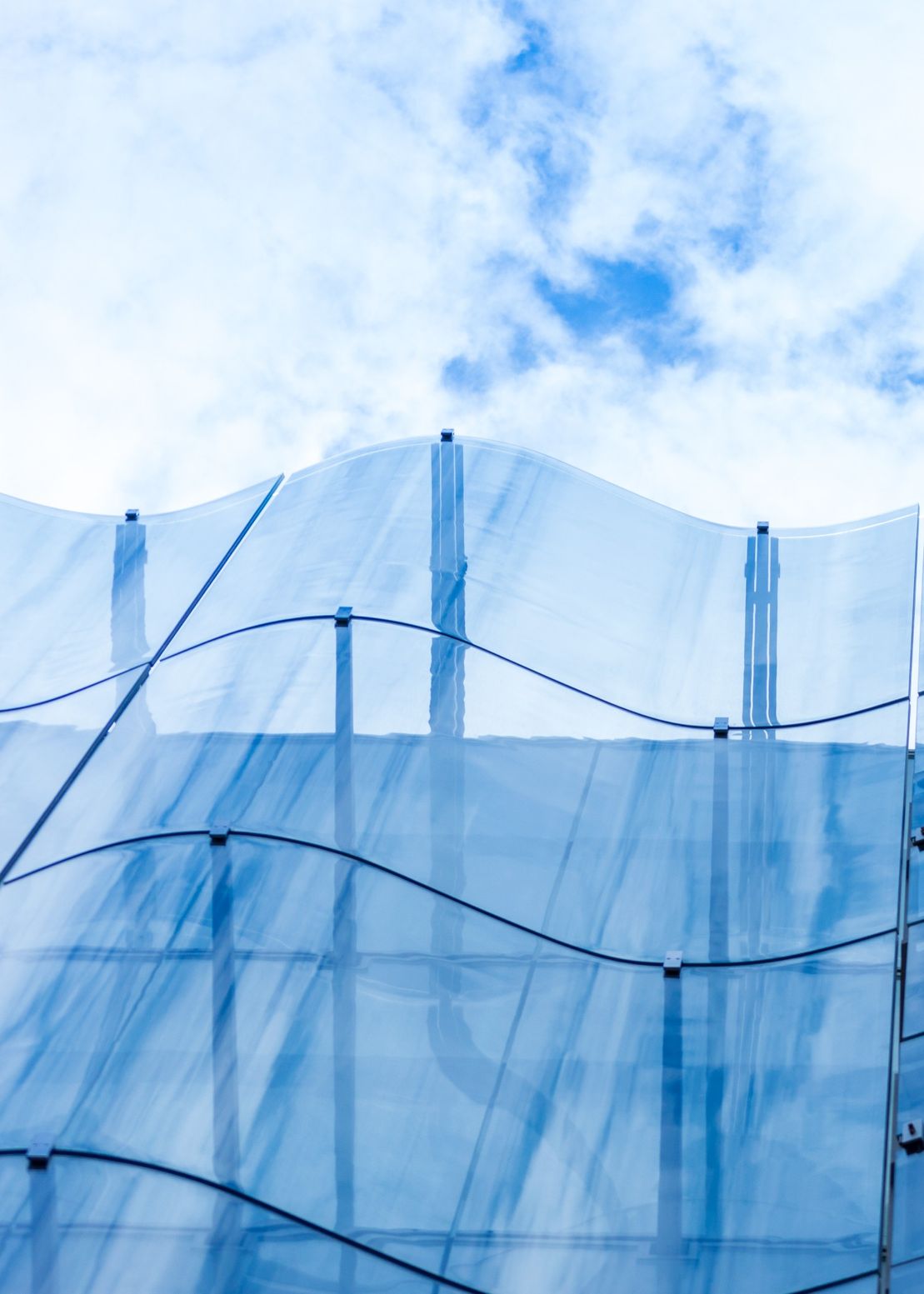 Detalle de la fachada de muro cortina de vidrio ondulado de un bonito edificio moderno, cielo y nubes reflejándose en él